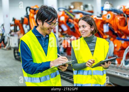 Multicultural male and female engineers smiling while controlling the assembly line of a robotic arms factory Stock Photo