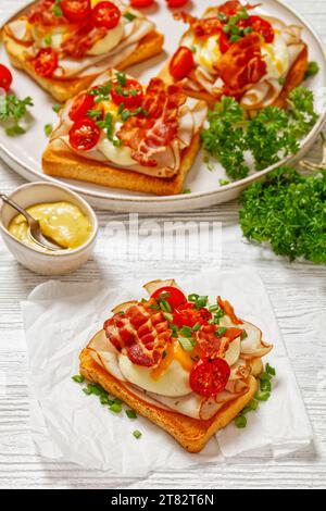 close-up of Kentucky Hot Brown, open sandwiches with ham, mornay sauce, cheddar cheese, topped with fried slices  of bacon and grilled cherry tomatoes Stock Photo