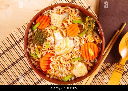 Top view of stir-fry noodles with vegetables in brown bowl placed on bamboo mat Stock Photo
