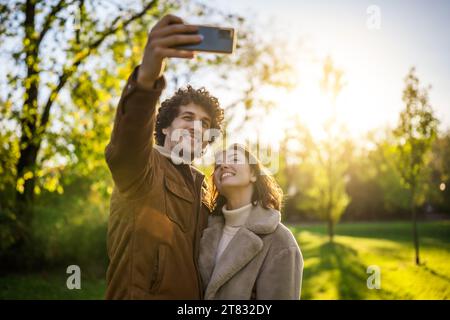 Portrait of happy loving couple in park in sunset. They are taking selfie. Stock Photo