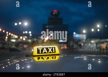 Selective focus on yellow taxi sign. Reflection in roof of car against airport terminal building at night. Stock Photo