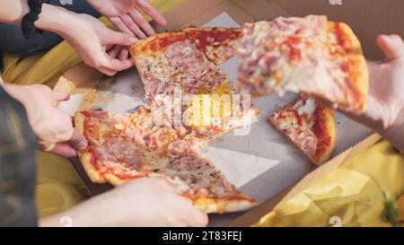 Young students' hands reach for the pizza. Stock Photo