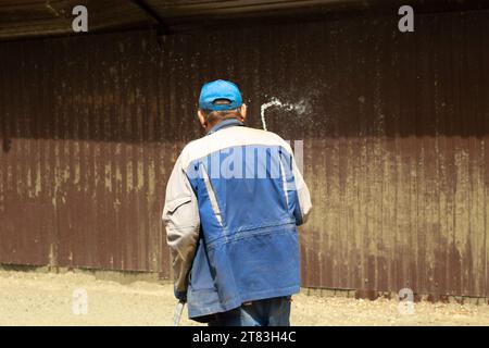 Worker washes dirt off fence. Water hose. Cleaning area. Sand laundering from steel fence. Man holding hose. Stock Photo