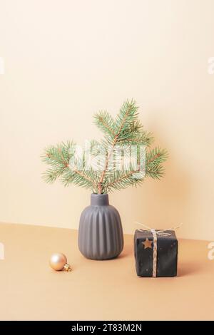 Spruce branch in ceramic vase, gift box and Christmas ball on beige table. Minimal Christmas concept. Stock Photo