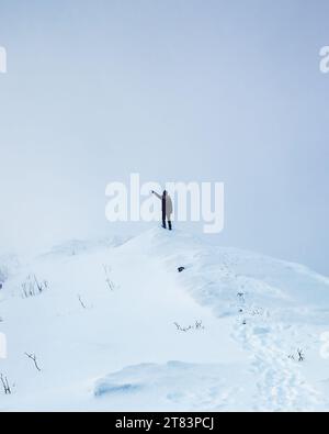 Hiker man standing and pointing on snowy mountain peak in gloomy weather Stock Photo