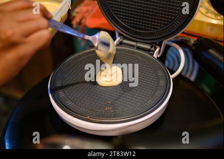 Homemade waffle pastry maker making and pouring batter dough on steel pan machine Stock Photo