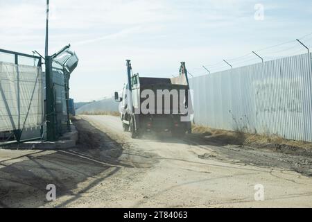 Truck is driving on road alone. Truck in industrial zone. Passage between fences. Transportation of waste. Stock Photo