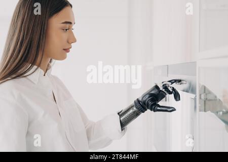 Focused woman using a sophisticated bionic hand to interact with a touchscreen, blending daily life with modern tech Stock Photo