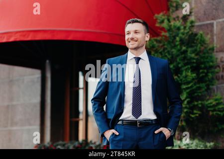 Confident businessman in a sharp suit smiling outside an upscale establishment with a red awning Stock Photo