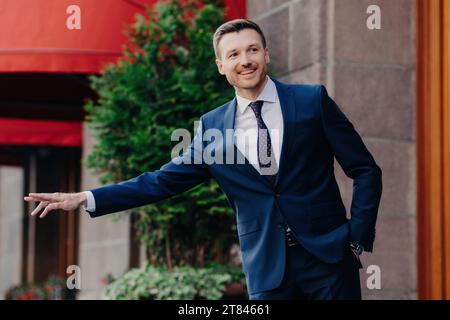 Cheerful businessman hailing a cab in a vibrant city setting, exuding confidence and style Stock Photo