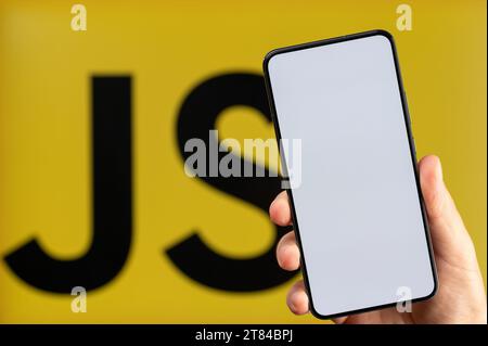 New York, USA - November 15, 2023: Creating new mobile app on JavaScript platform background with smartphone clean screen in hand Stock Photo