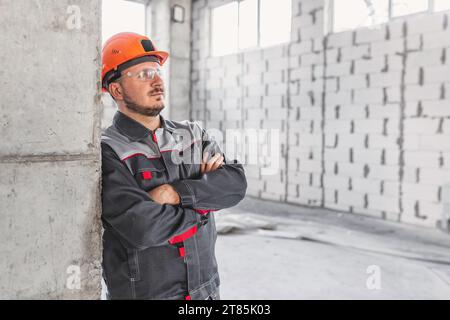 Worker in hard hat and protective glasses at a construction site near a reinforced concrete column, looking to the side, copy space Stock Photo