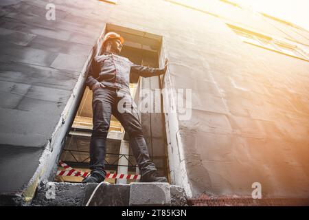 A handyman in overalls and a hard hat stands in the opening of a building under construction Stock Photo