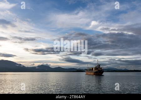 Old rusting cargo tanker sits anchored in beautiful remote port surrounded by mountains Stock Photo