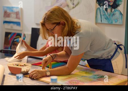 Inspired creative middle aged woman artist, art teacher during her work in art gallery or workshop. Female painter teaching a little student, developi Stock Photo