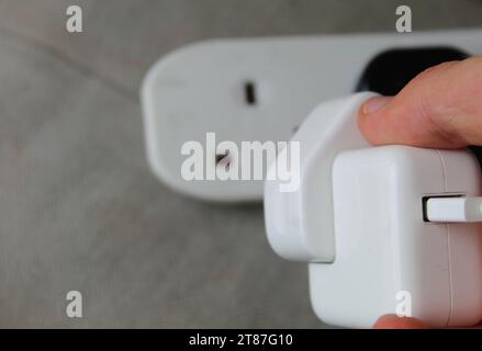 A photo of someone plugging in an electrical smartphone charger plug into a portable electric socket. Stock Photo