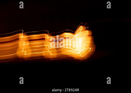 Abstract light painting of parallel light trails that dance across the image. Golden yellow highlights and warm orange tones. Stock Photo