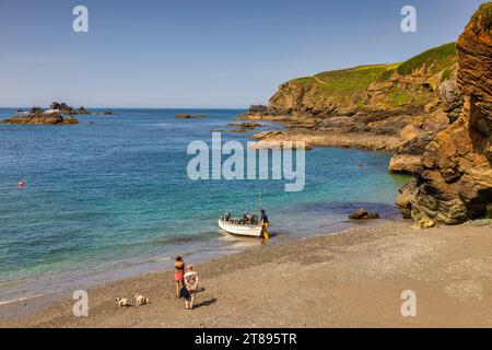22 May 2023: Lizard Cove, Cornwall, UK - Small cove at The Lizard, with man launching a boat and tourist with two dogs. Perfect spring day. Stock Photo