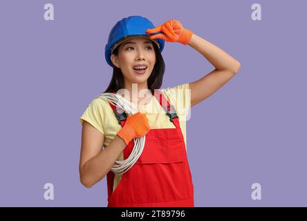 Young female electrician with cables on purple background Stock Photo