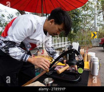 Thai roadside barista pulls an espresso shot using a portable lever press machine in Chiang Mai on17 February 2023. Stock Photo