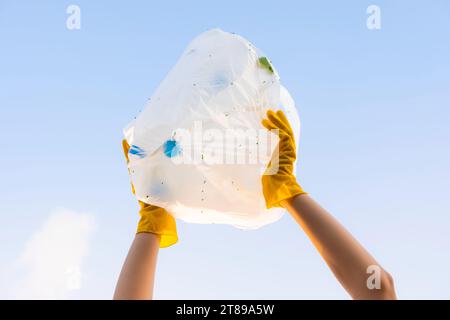 A young volunteer's hand raises a garbage bag of plastic bottles into the sky. On World Environment Day Stock Photo