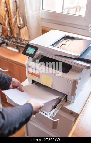 Woman putting paper in a printer to make photocopies and teleworking from home. Stock Photo