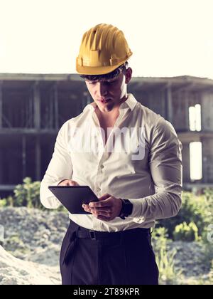 A man wearing a hard hat and holding a tablet in costruction site Stock Photo