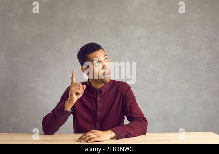 Young african american man sitting at table with raised finger having idea Stock Photo