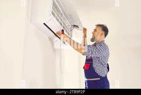Professional electrician man with screwdriver maintaining modern air conditioner indoors. Stock Photo