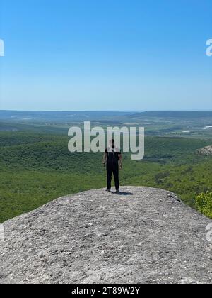 a man stands on a mountain and looks into the distance under a blue sky hiking journey Stock Photo