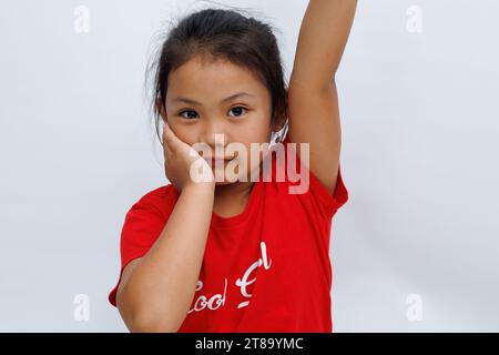 An Asian little girl raises her left hand straight up trying to ask permission from her teacher to answer a question while smiling and confident. cute Stock Photo