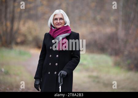 Portrait smiling beautiful elderly woman with white hair against background of autumn nature forest. Positive middle aged female model looks at camera Stock Photo