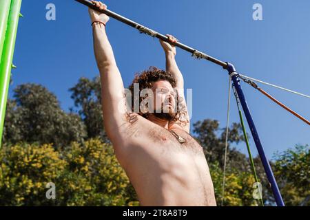 Curly and bearded man doing pull-ups on horizontal bar Stock Photo