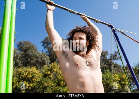 Curly and bearded man doing pull-ups on horizontal bar Stock Photo