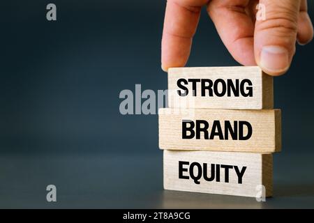A symbol of the values of a strong brand. Business concept, words Strong Brand Equity on wooden blocks. The hand of a businessman. Beautiful navy blue Stock Photo