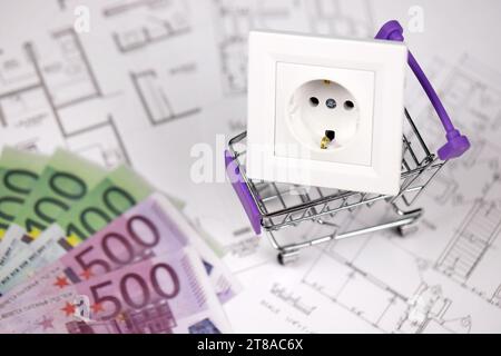 European standard EU outlet in small shopping cart on blueprints of residential house plan close up. Concept of shopping and electricity devices Stock Photo