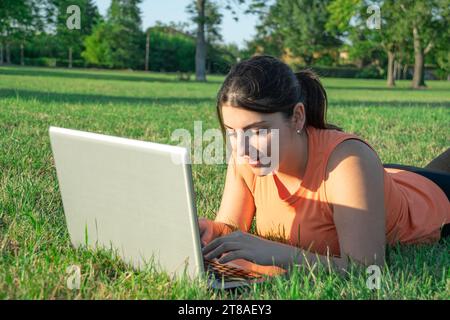 Young Caucasian woman lying on park using her laptop very happy Stock Photo