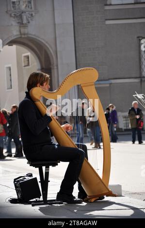 SALZBURG, AUSTRIA - MARCH 9, 2012: Street performer musician beggar playing on harp stringed musical instrument in Salzburg old city Stock Photo
