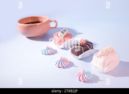 Coffee and Confections: A Pink Cup of Coffee with Mini Petite Four Decorated Cakes and Meringue Candy on Blue Background, Easter Treats, Bakery Concep Stock Photo