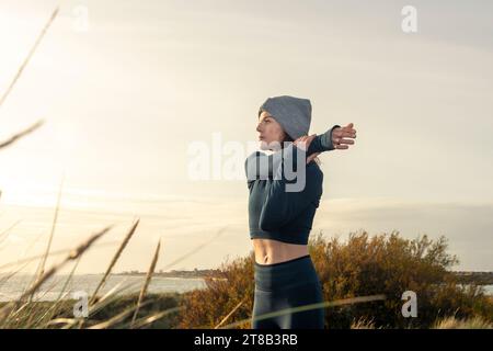 Fit, sporty woman doing an arm stretch outside at sunrise. Stock Photo