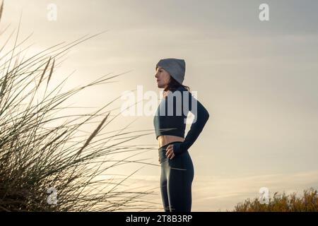 side view of a sporty woman with her hands on her hips resting after exercising outdoors, autumn, winter fitness series. Stock Photo