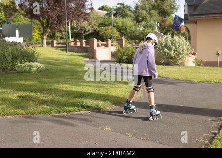 a child learns to roller skate in the park a dressed girl in a lilac sweater Stock Photo