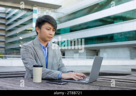 Asian entrepreneur man working online focused on laptop sitting outdoor Stock Photo