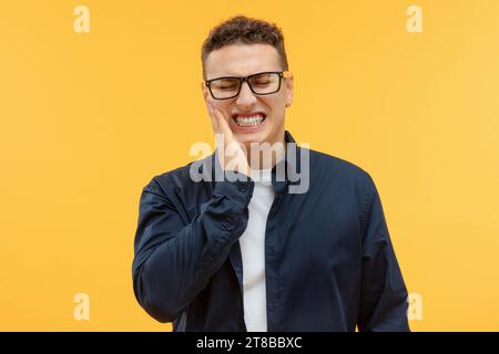 Unhappy young guy holding hand on cheek Stock Photo