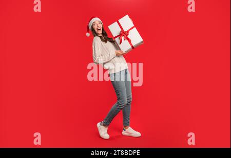 woman in Santa hat holding festive gift on red background Stock Photo