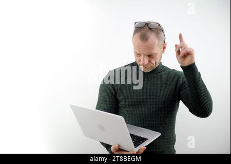 Student using laptop isolated on white. a man in a green sweater, an adult, raised his finger up, put glasses on his forehead, looks in surprise at a laptop on a white background High quality photo Stock Photo