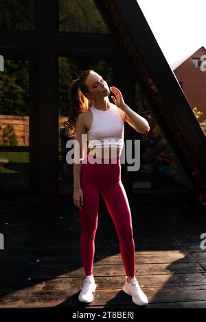 Athletic young redhead girl, wearing in sportswear, sitting on the pink ...