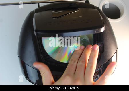 A top down photo of someone slotting a cd into a black cd player on a white desk. Stock Photo