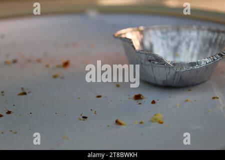 A photo of an empty silver mince pie tin on a white plate covered in crumbs on a white desk. Stock Photo