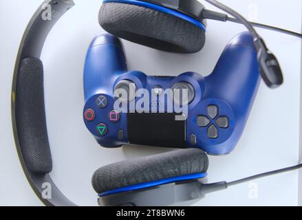 A photo of a dark blue Playstation gaming console controller and a pair of headphones on a white table. Gamer. Stock Photo